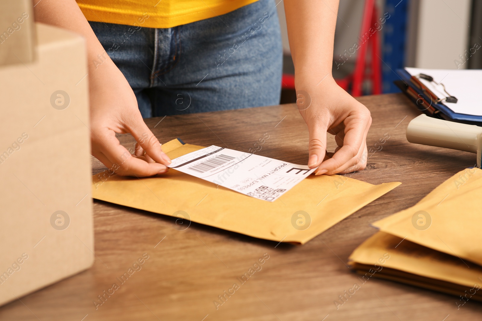 Photo of Post office worker sticking barcode on parcel at counter indoors, closeup