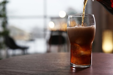 Photo of Pouring cola into glass on table against blurred background. Space for text