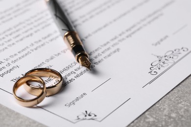 Marriage contract, fountain pen and golden wedding rings on grey table, closeup