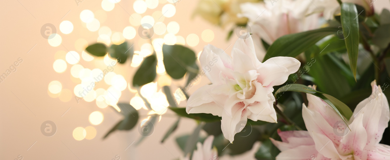 Photo of Bouquet of beautiful lily flowers against beige background with blurred lights, closeup. Space for text