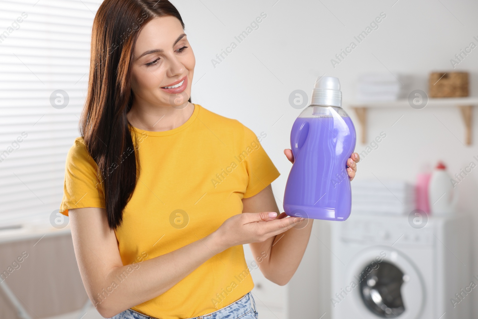 Photo of Beautiful woman showing fabric softener in bathroom