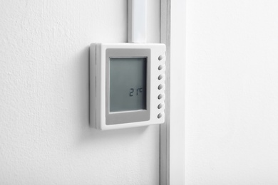 Photo of Modern thermostat on white wall. Heating system