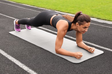 Photo of Young woman doing plank exercise at stadium