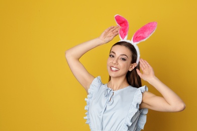 Photo of Portrait of beautiful woman in Easter bunny ears headband on color background, space for text