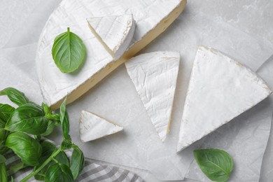 Photo of Delicious brie cheese with basil on light grey table, flat lay