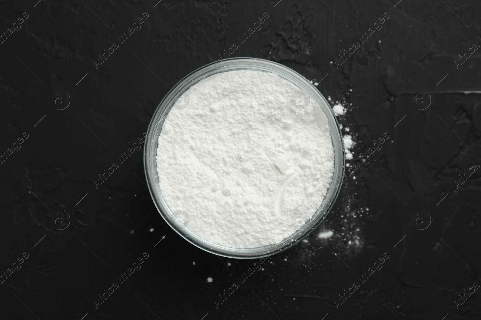 Photo of Baking powder in bowl on black textured table, top view