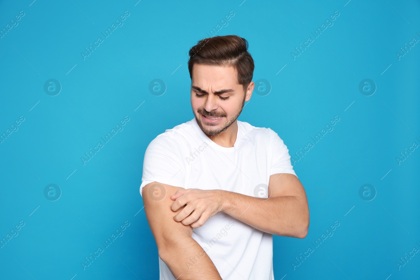 Photo of Young man scratching arm on color background. Annoying itch