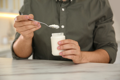 Photo of Young man with tasty yogurt at white marble table, closeup