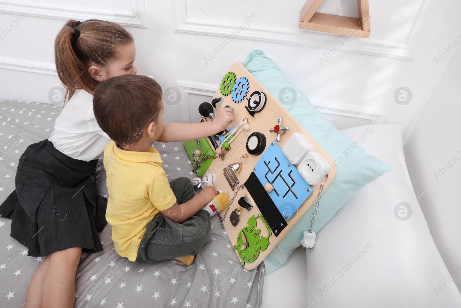 Photo of Little boy and girl playing with busy board on bed in room