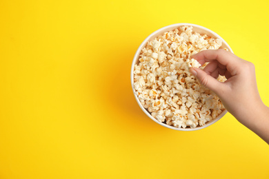 Photo of Woman taking fresh pop corn from bucket on yellow background, top view. Space for text