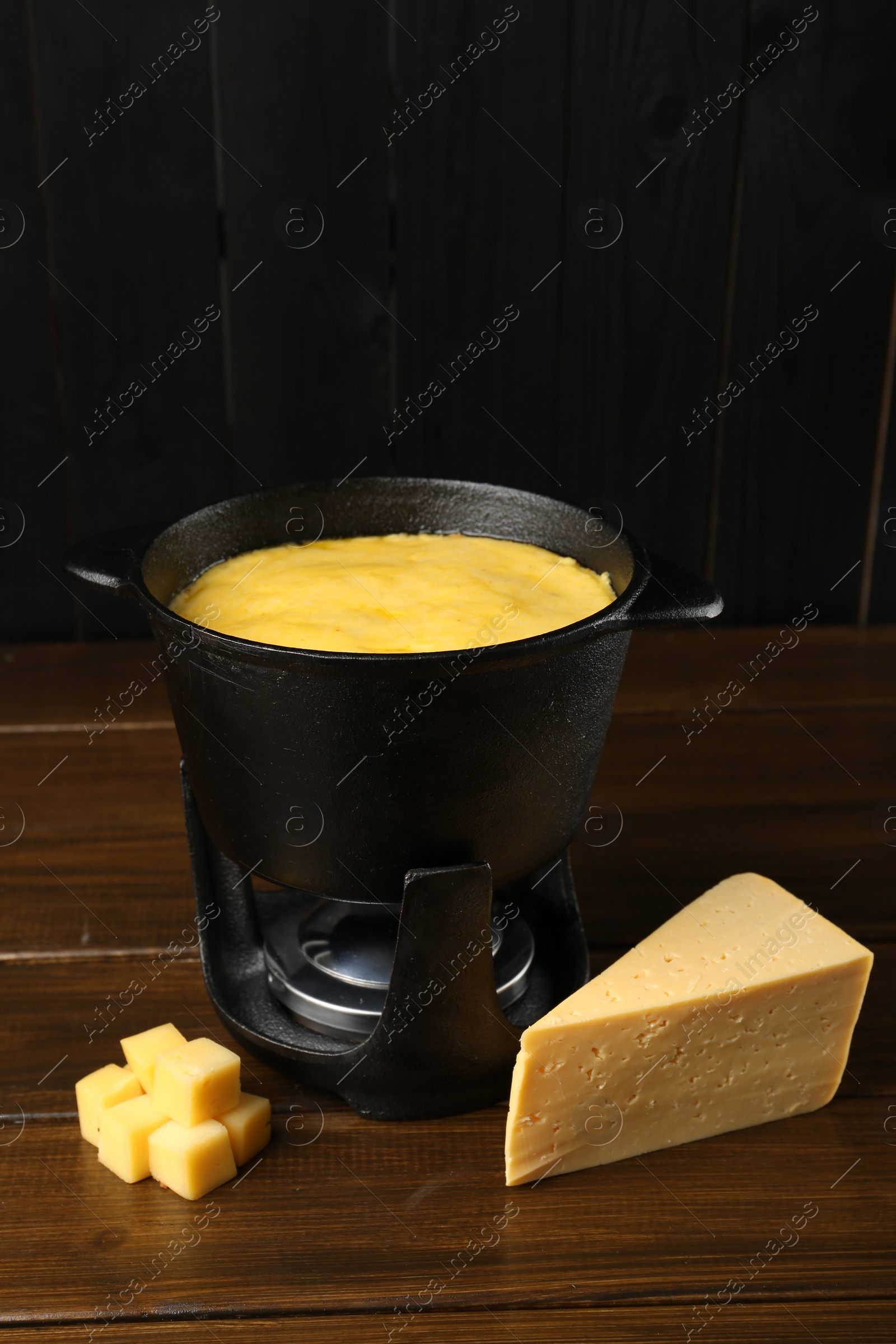 Photo of Fondue pot with melted cheese and pieces at wooden table