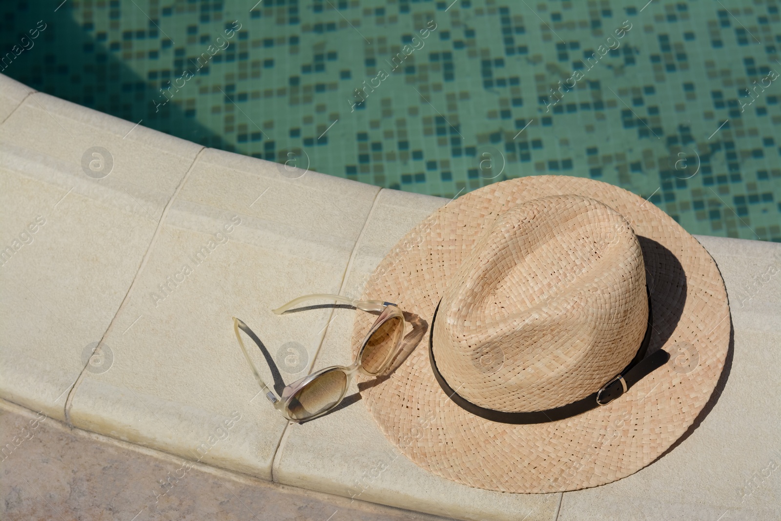 Photo of Stylish hat and sunglasses near outdoor swimming pool on sunny day, space for text. Beach accessories