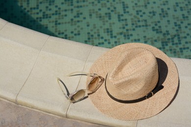 Stylish hat and sunglasses near outdoor swimming pool on sunny day, space for text. Beach accessories