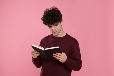 Teenage boy reading book on pink background