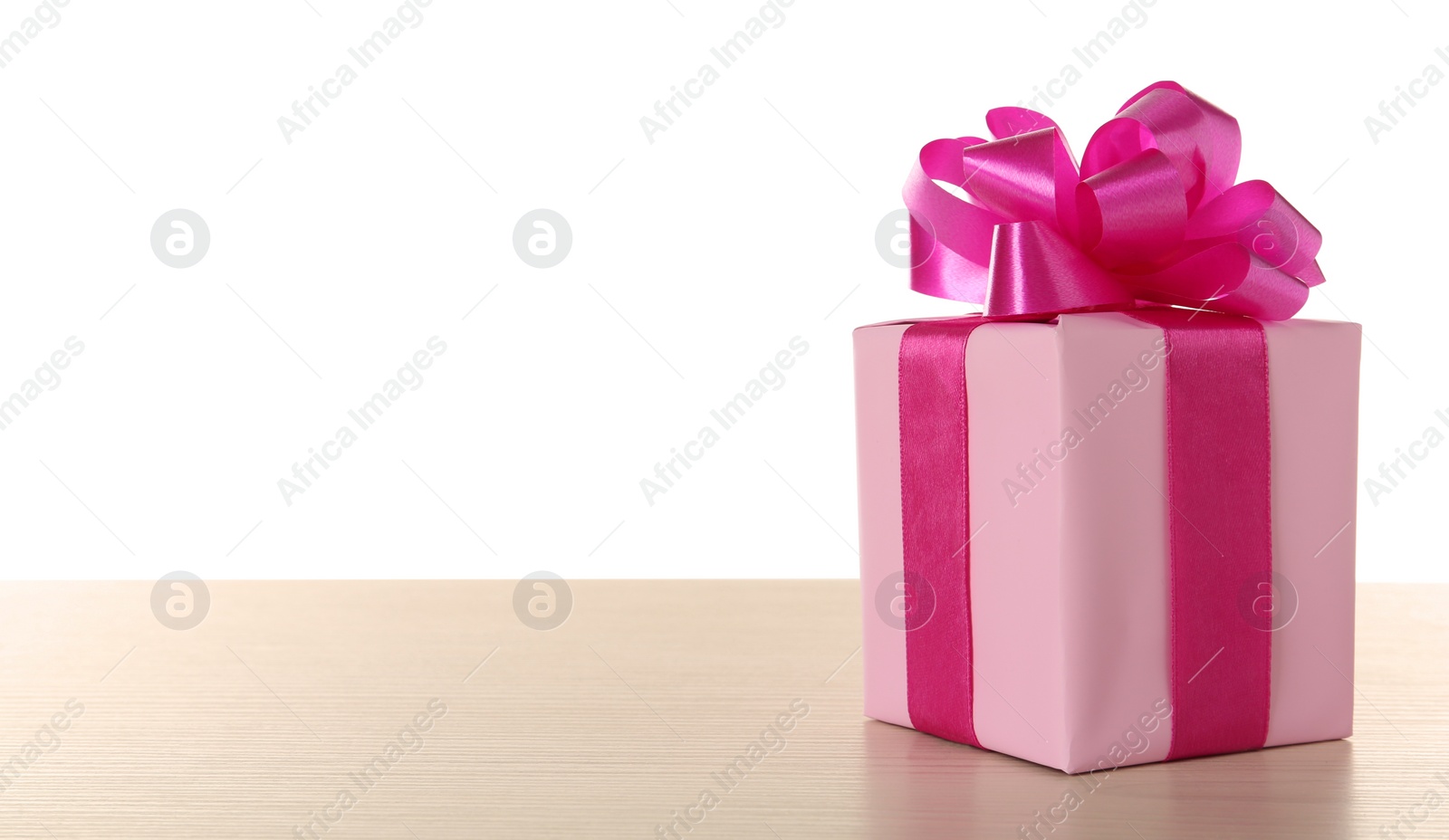 Photo of Beautifully wrapped gift box with pink bow on wooden table against white background, space for text