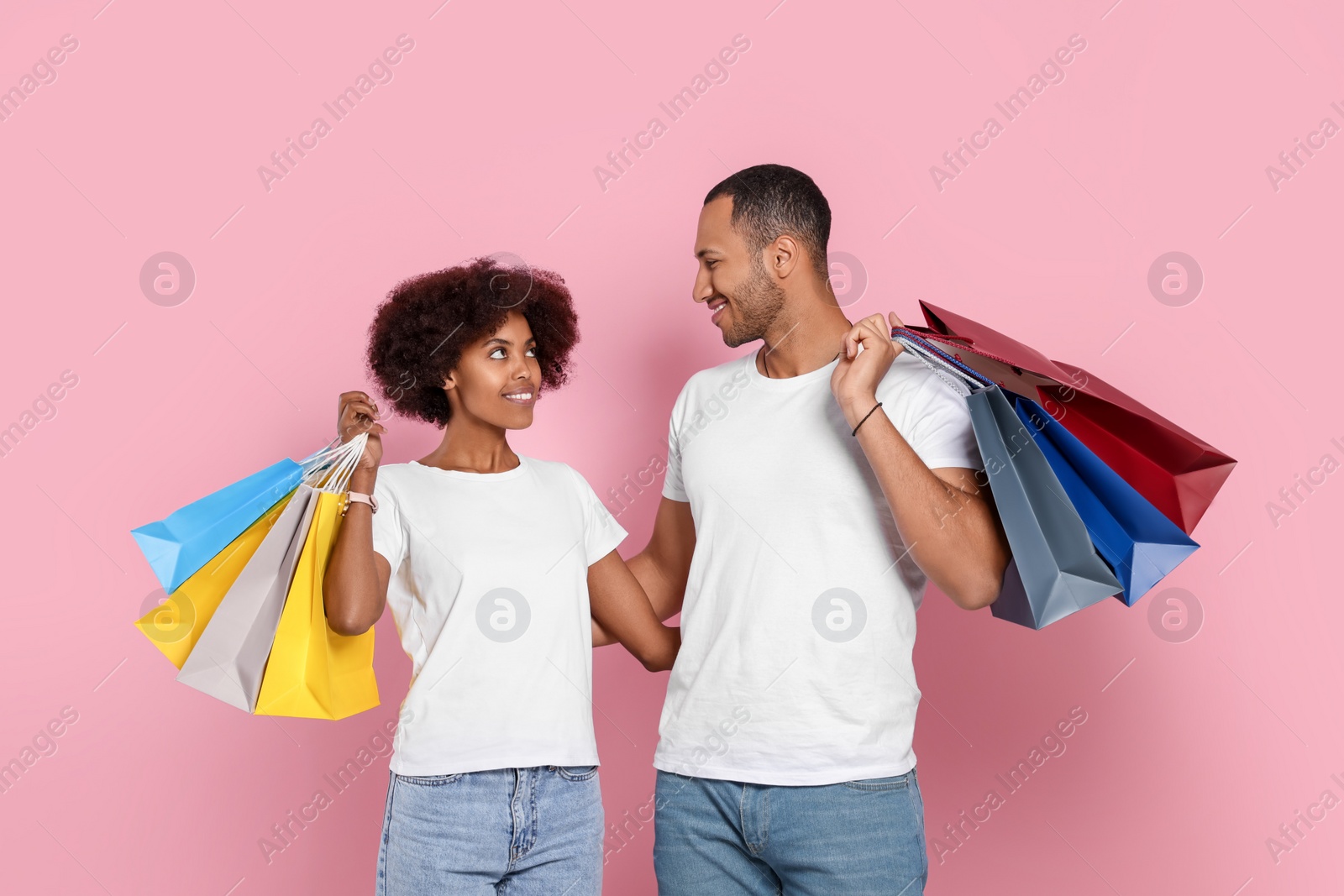 Photo of Happy African American couple with shopping bags on pink background