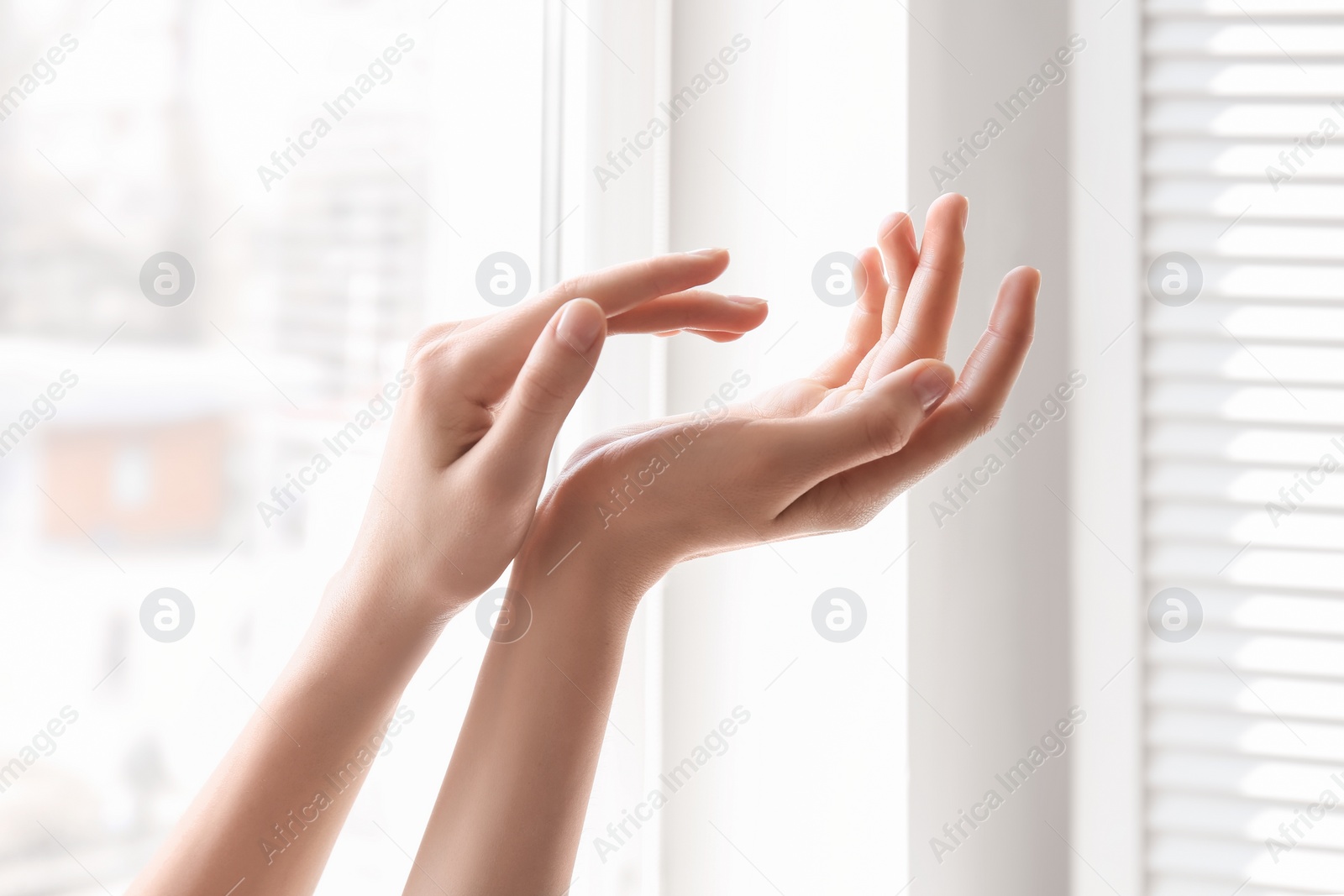 Photo of Young woman against window. Focus on hands moisturized with cream