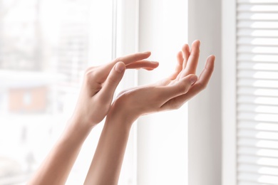 Young woman against window. Focus on hands moisturized with cream