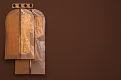 Photo of Garment bags with clothes hanging on brown wall. Space for text