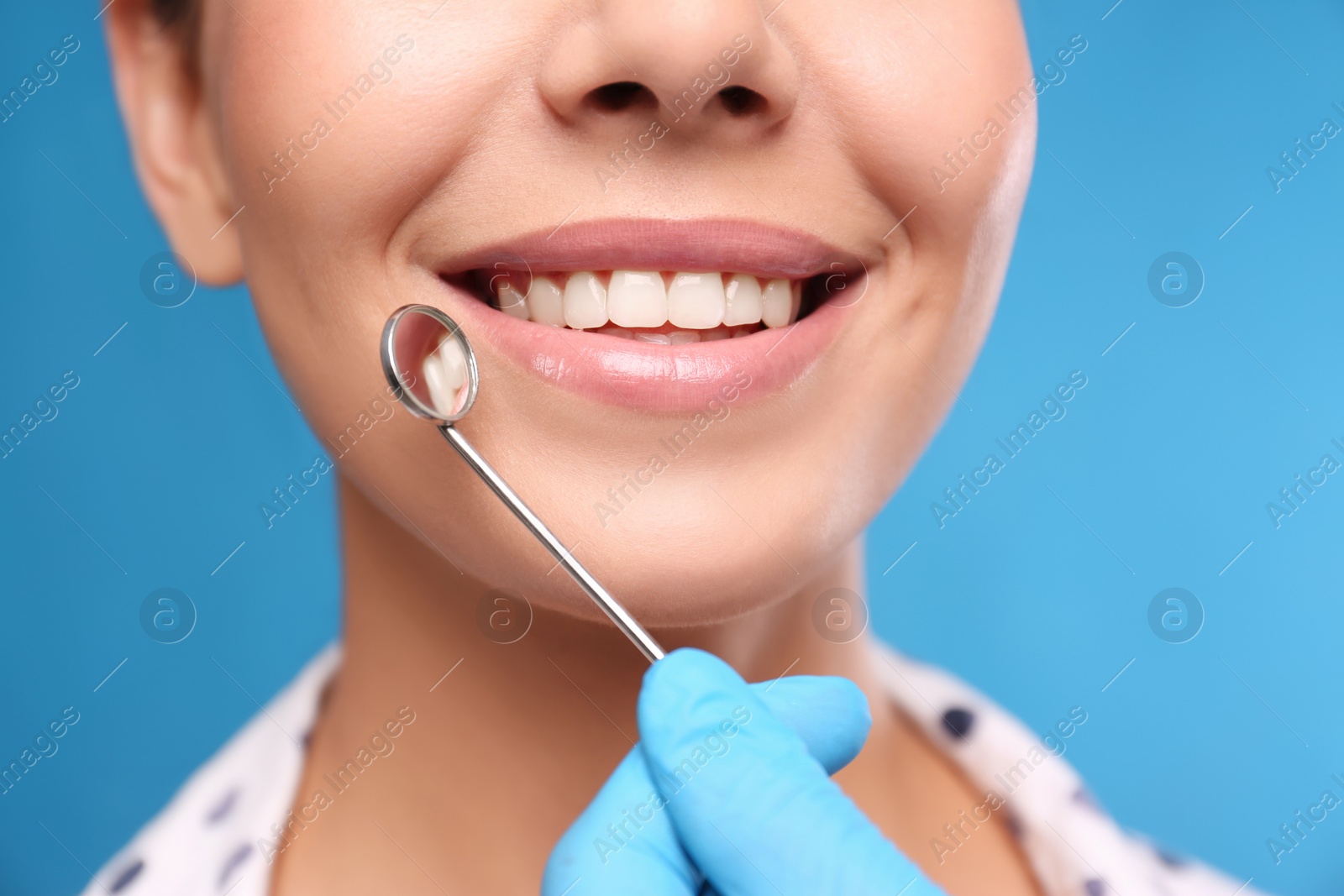 Photo of Doctor examining woman's teeth on blue background, closeup. Cosmetic dentistry