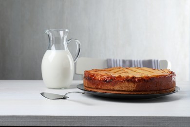 Photo of Tasty apricot pie and jug of milk on white wooden table