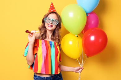 Young woman with bright balloons and party blower on color background. Birthday celebration