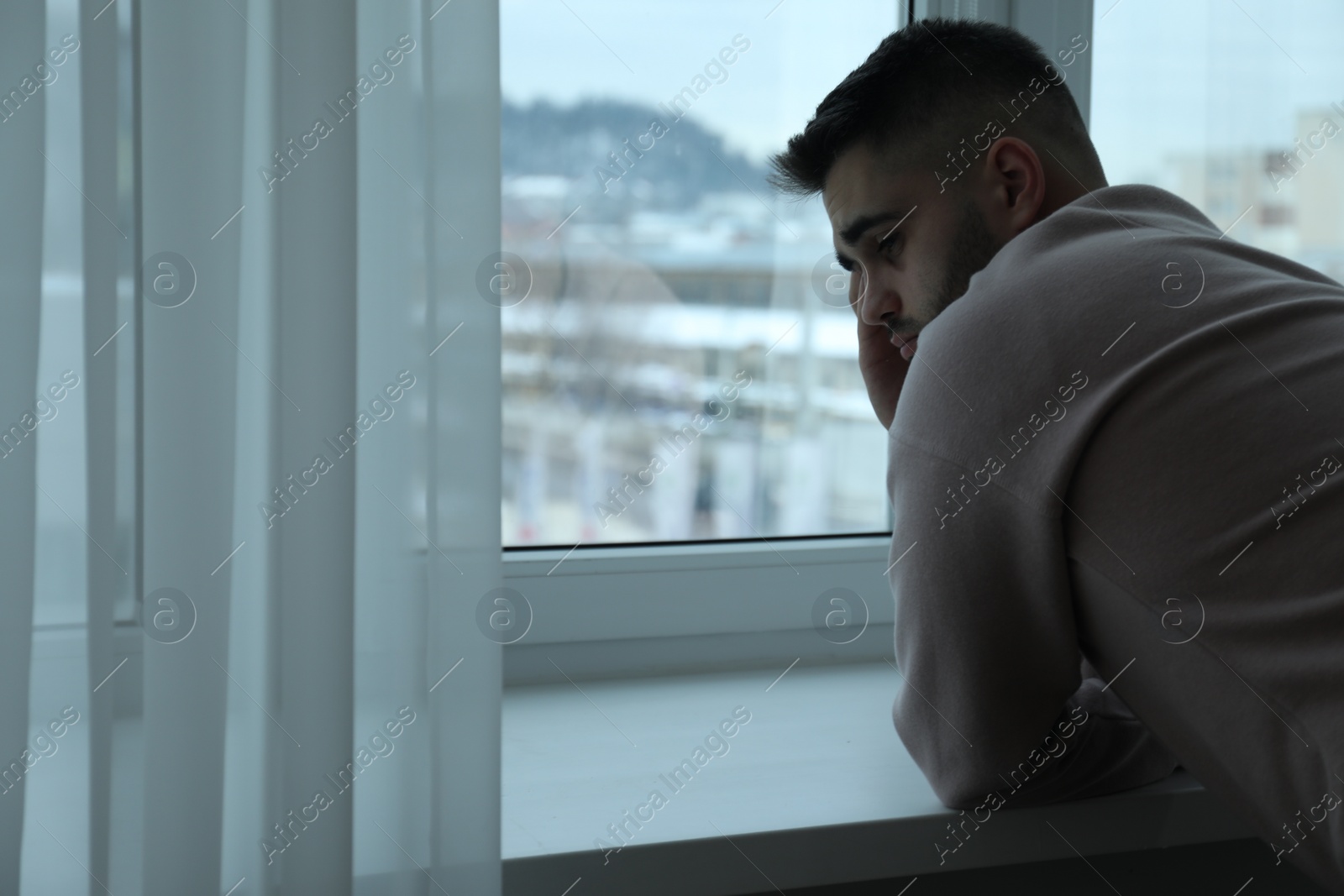 Photo of Sad man near window at home. Space for text