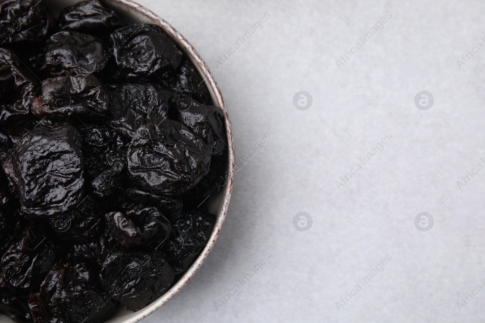 Photo of Sweet dried prunes in bowl on light table, top view. Space for text