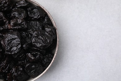 Photo of Sweet dried prunes in bowl on light table, top view. Space for text