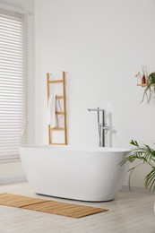 Stylish bathroom interior with ceramic tub and terry towel on wooden shelf