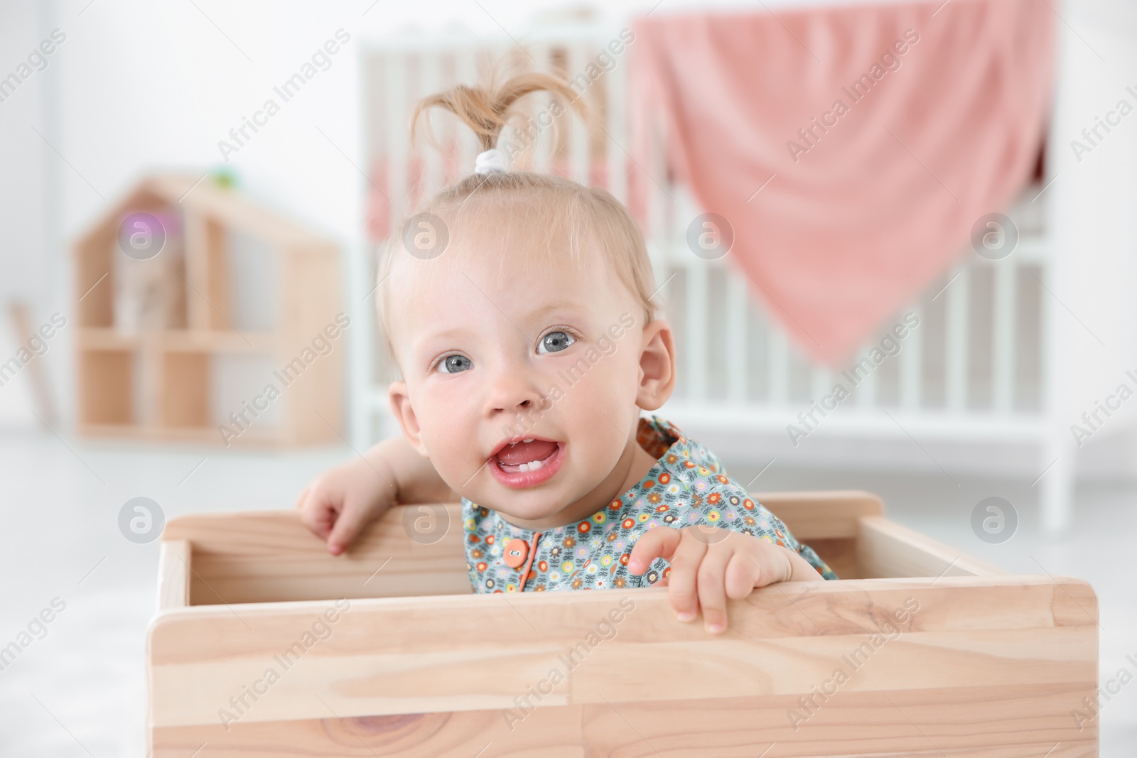 Photo of Adorable baby girl playing in wooden cart at home