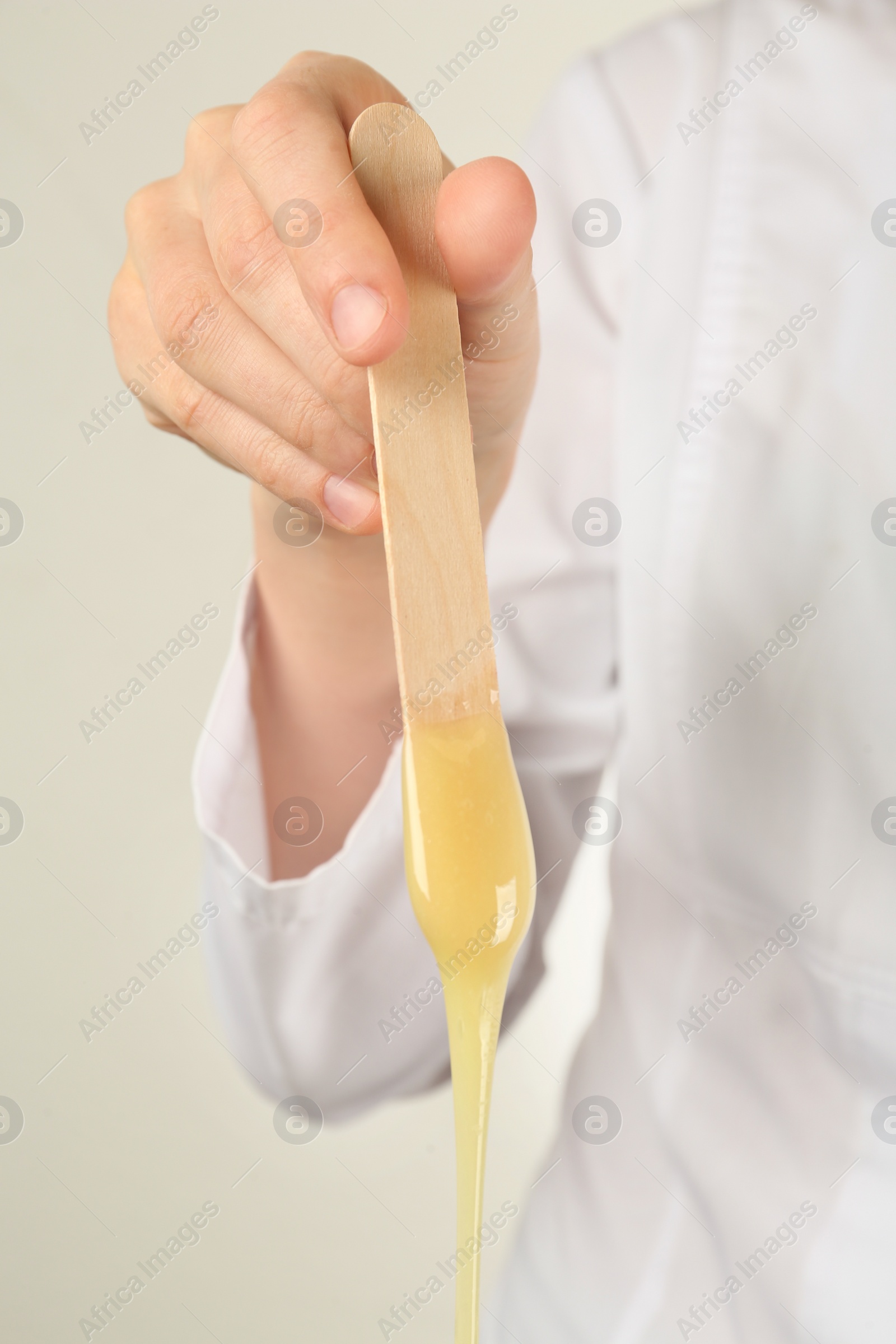 Photo of Woman holding spatula with hot depilatory wax, closeup