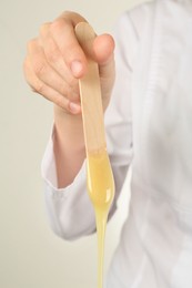 Photo of Woman holding spatula with hot depilatory wax, closeup