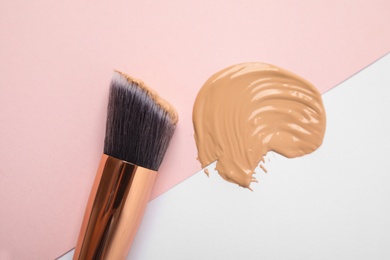 Photo of Sample of liquid foundation and makeup brush on color background, top view