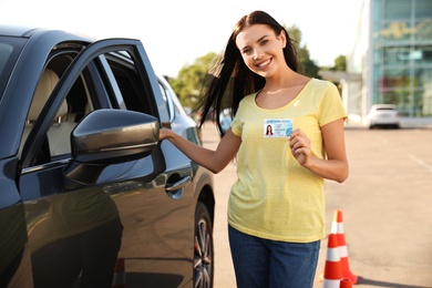 Photo of Happy young woman holding license near car outdoors. Driving school