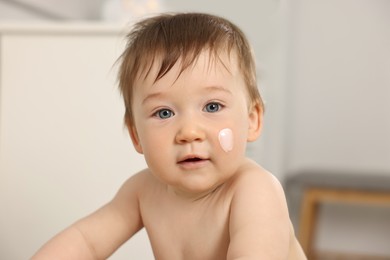 Cute little baby with moisturizing cream on face indoors