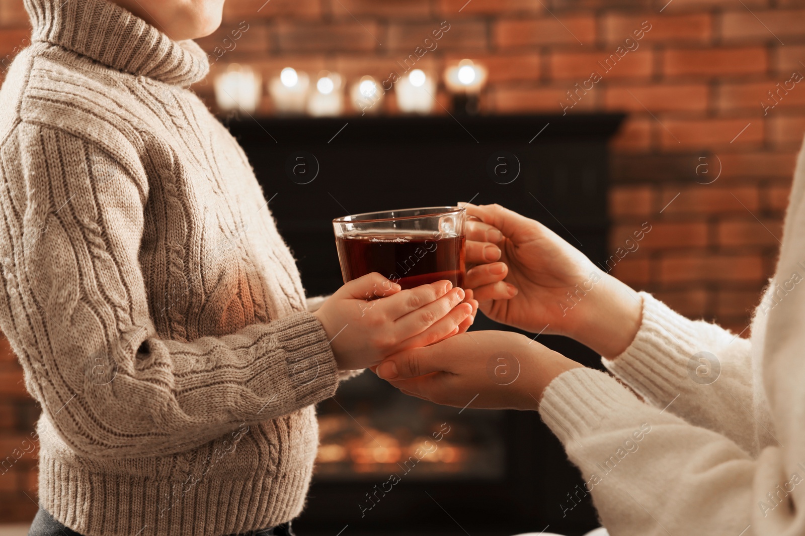 Photo of Mother and son with cup of tea near fireplace at home, closeup