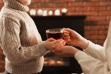 Mother and son with cup of tea near fireplace at home, closeup