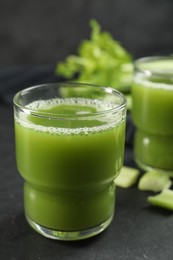 Photo of Glasses of delicious celery juice and vegetables on black table, closeup