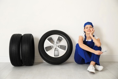 Female mechanic with car tires on light wall background