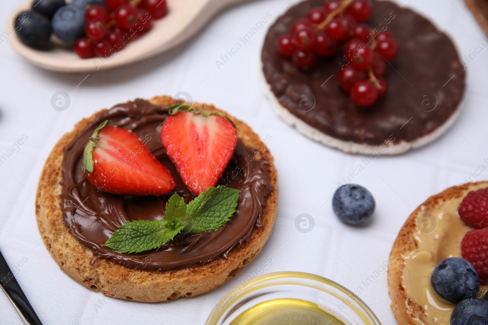 Photo of Fresh rice cake and rusks with different toppings on white table, closeup