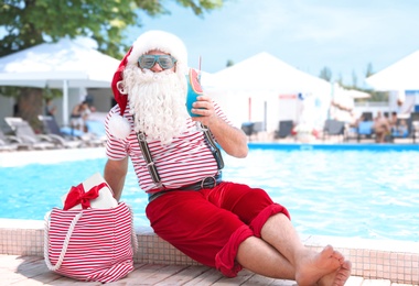 Photo of Authentic Santa Claus with cocktail and gift in bag near pool at resort