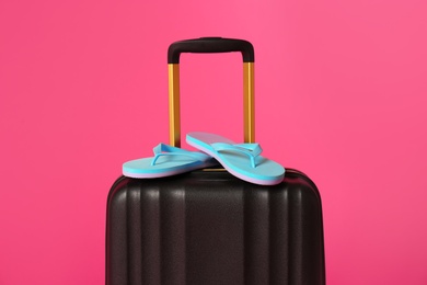 Photo of Stylish suitcase with flip flops on color background