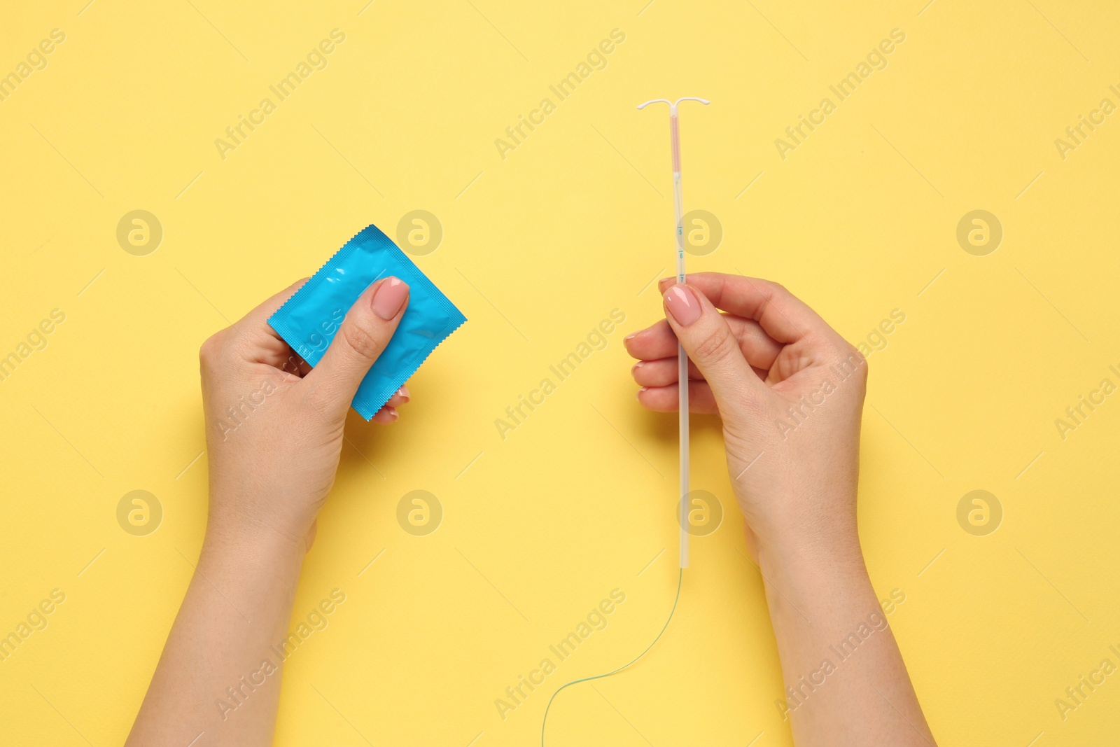 Photo of Woman with condom and intrauterine device on yellow background, top view. Choosing birth control method