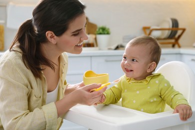 Photo of Mother feeding her cute little baby in kitchen