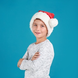 Image of Happy little child in Santa hat on light blue background. Christmas celebration