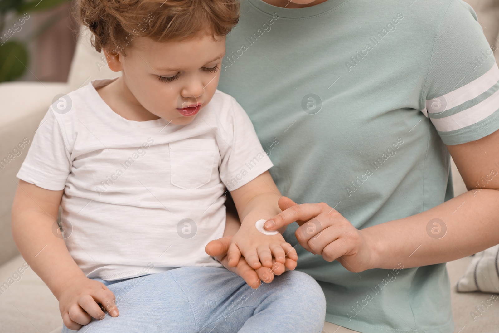 Photo of Mother applying ointment onto her son`s hand indoors