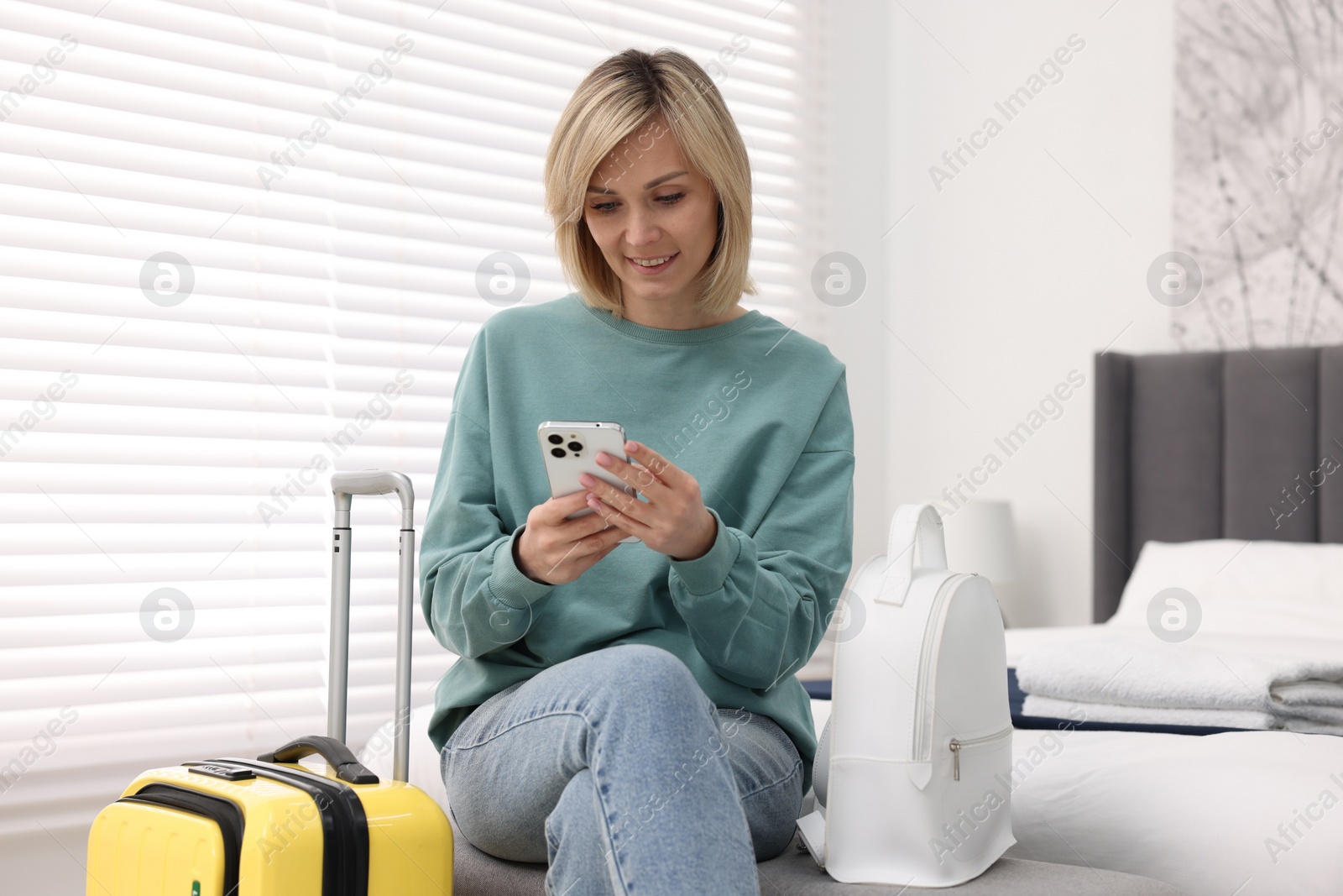 Photo of Smiling guest with smartphone in stylish hotel room