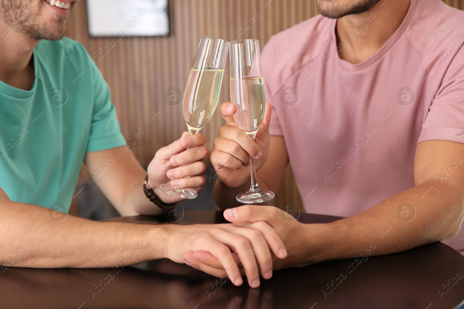 Photo of Gay couple with glasses of champagne at table indoors, closeup