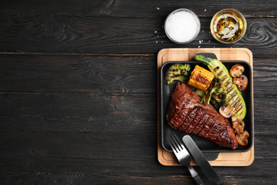 Photo of Delicious beef tenderloin served on black wooden table, flat lay. Space for text